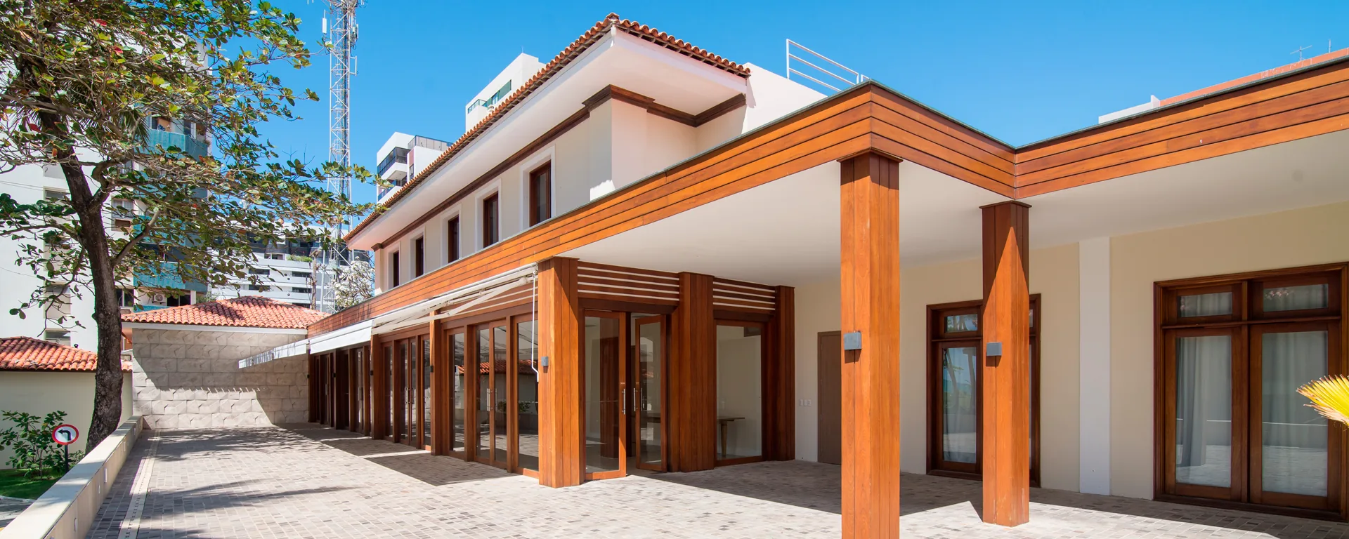 Fachada do centro de eventos do Hotel Jatiúca, com pergolado de madeira, portas de vidro em fita e pátio pavimentado