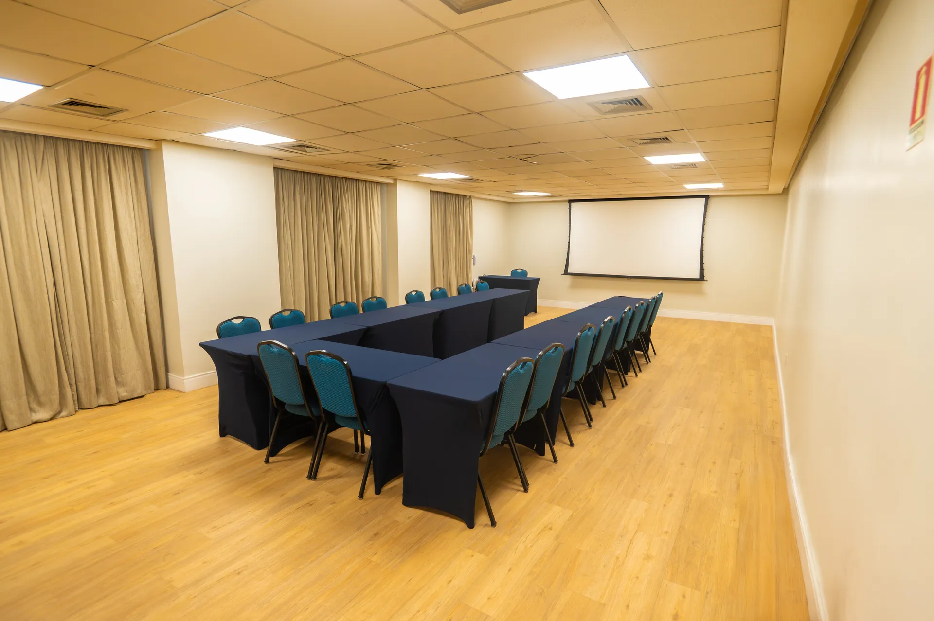 Salão Francês montado em mesa em U, com piso de madeira e tela de projeção